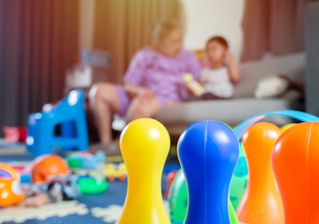 Cropped image of colorful bowling with blurred image of lots of toys and Asian boy with a grandmother sitting happily on the fosa in the background. Family happiness conceptの写真素材