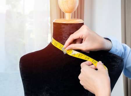 Close up hands of young Asian female fashion designer taking measurements on mannequin in her studioの写真素材