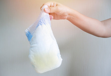 Selective focus. Mother hand holds dirty used diaper for garbage. Parent takes care of baby health and environment at home.の写真素材
