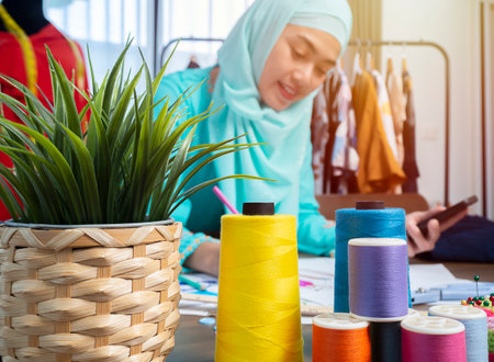Happy smiling Asian muslim woman designer as a startup business owner working in her tailor shop. Work from home concept.の写真素材