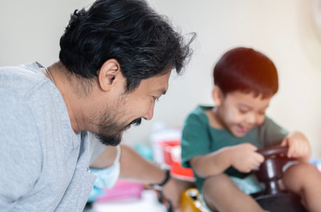 Asian dad sitting on floor playing with toddler son with toy cars at home, happy caring black father have fun with little kid engaged in funny activity race on automobiles.の写真素材