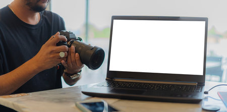 Handsome young photographer using a camera while working with a laptop with blank screen for your design in cafeの写真素材