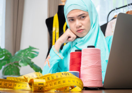 Young Muslim woman seller checking clothes details in store and writing data in computer labtop with a serious face. Ideas work planning concept.の写真素材
