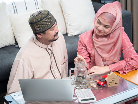 New happy muslim couple looking at each other and putting coins  in a jar glass for save their money.  Man and Women couple saving money for family and home. Savings conceptの写真素材