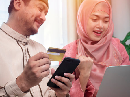Online Shopping. Happy muslim couple using digital tablet and credit card buying and purchasing things sitting on sofa at home. Joyful customers, modern shopping and sales concept.の写真素材