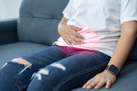 Woman in painful expression holding hands against belly suffering menstrual period pain, lying sad on home bed, having tummy cramp in female health conceptの写真素材