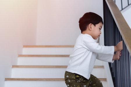 Cropped image of little Asian boy move and climb wood stairs down with handle the railing carefully. Concept carefully search new expectations, education children kid goodsの写真素材