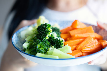 Cropped image of young woman dressed in white t-shirt showing broccoli and carrot in a plate to camera. Healthy eating concept.の写真素材
