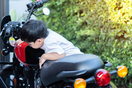 Beautiful attractive Asian boy  try to climb up to big motorcycle at natural day background. Motorcycles, speed, movementの写真素材