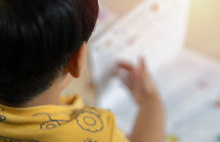 Cute little Asian boy reading book on floor at home, back view. Learning concept.の写真素材