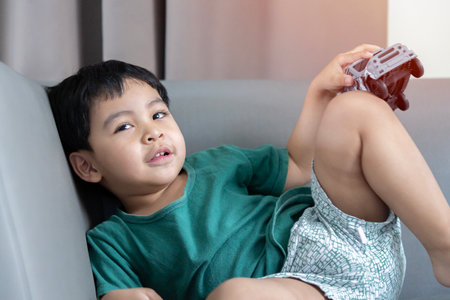 Portrait of Asian kid in casual wear dreaming about real car, and looking up. Child boy holding gray toy car in hands, having fun, excited.の写真素材