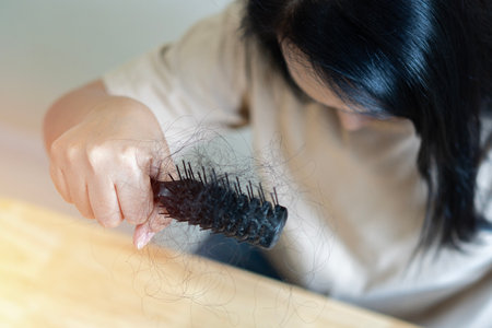 Young Asian woman with comb and problem hair on light beige background. Hair care and beauty concepts.の写真素材
