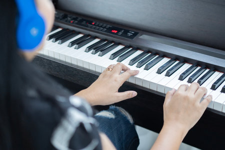 Young woman wearing headphones for recording a song and playing synthesizer during rehearsal of her band in a professional studio. Piano keyboard with headphones for music concept.の写真素材