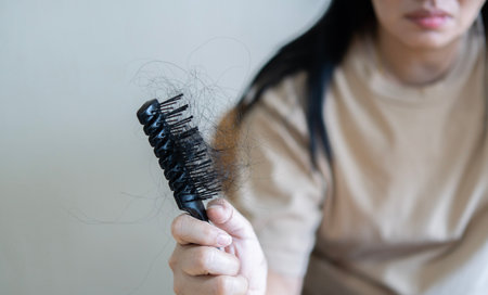 Selective focus. Asian girl with a comb and problem hair on light beige background. The problem of hair loss concept.の写真素材