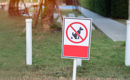 Warning label "No Dog Pooping" on the public park background. No dog pooping sign on a park lawn, with copy space.の写真素材