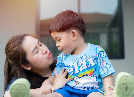 Beautiful woman and her cute little son are kissing and smiling at home outdoor background. Happy harmonious family outdoors concept.の写真素材