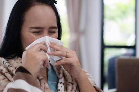 An Asian woman covered with blanket blowing running nose got fever caught cold sneezing in tissue...