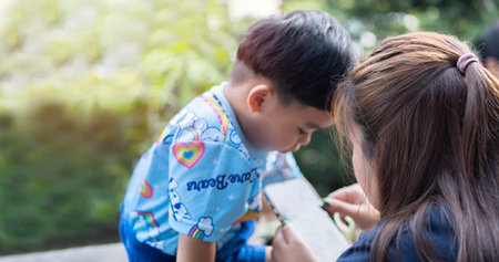 Asian young mother and baby playing with a smart phone and sitting on a chair in the garden at home.  Concept of children developmentの写真素材