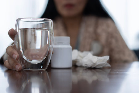 Cold medicine and sick woman drinking hot beverage to get well from flu, fever and virus. Dirty paper towels and tissues on table. Selective focus.の写真素材