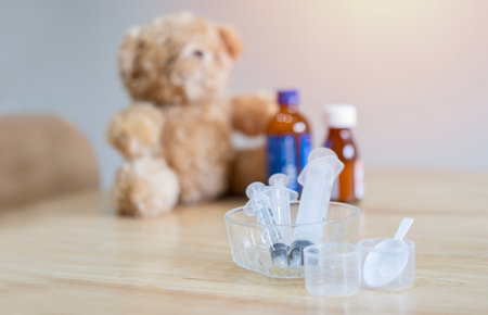 A glass bowl filled with many syringe on the burred background of a teddy bear with child medicine bottles. The concept of treatment of diseases for kids.の写真素材