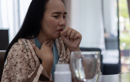 Sick young Asian woman in brown blanket coughing covering mouth with hand keeping eyes. Healthy lifestyle ill sick disease treatment cold season conceptの写真素材