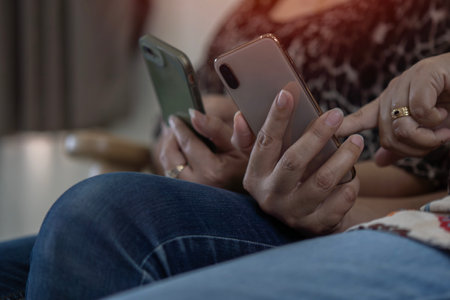 Close up group adult friends sitting on sofa and using hands modern smartphone. People working together concept. Selective focus.の写真素材
