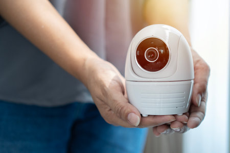 Security camera baby monitor in hand on Asian woman hands with sunlight passing through the window. Home security concept.の写真素材
