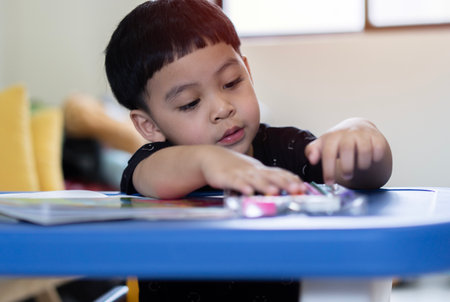 Cute little boy doing homework, reading a book, coloring pages, writing and painting. Children paint. Kids draw. Preschooler with books at home.の写真素材