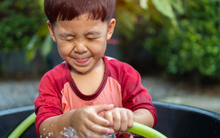 Head portait of Asian little boy has fun playing water splash. Healthy activity for hot sunny day. Kids playing water concept.の写真素材