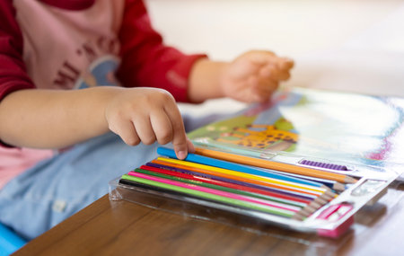 Cropped image of a little boy sitting and  pickup a blue color pencil for drawing to coloring book. Soft focus and selective focus.の写真素材