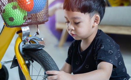 Little Asian cute boy learning to repair a bike and to change a wheel on warm sunny day.  Active leisure with kids.の写真素材