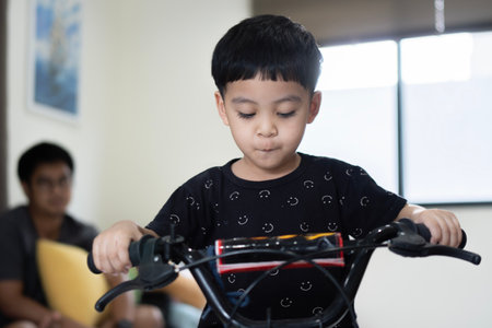 The boy purposely learns to ride a bicycle in the house, while his father was watching nearby. Concept of a happy childhood.の写真素材