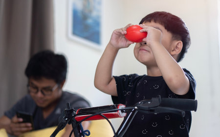 The Asian boy had fun learning to ride a bicycle and play with toy in the living room with the background is a blurred image of his father.の写真素材