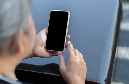 Senior woman hand holding phone black screen on black stone table background. Selective focusの写真素材