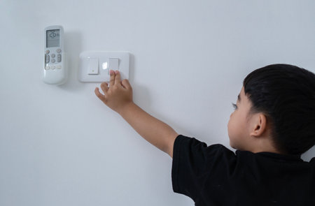 Back view at little careless child boy exploring house playing turning light switches, home electricity danger security, electric shock risk and kids safety, energy power saving concept, copy spaceの写真素材