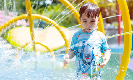 Happy boys run under the spray from the fountain in the park on a hot summer day. Children walk in the parkの写真素材