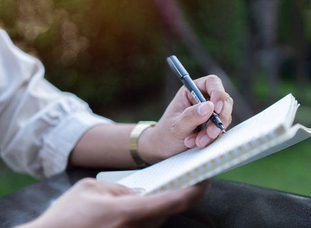 Asian man hands with pen writing on notebook in park. Writing notebook diary, working from anywhere...