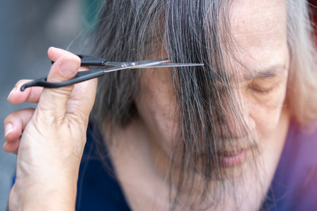 Hands of a young hairdresser cutting the hair of an old Asian lady. Lifestyle. Top view, selective focus.の写真素材