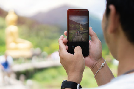 Back view of cropped Asian man tourist taking photo with a smartphone at the temple on vacation Bangkok Thailand.の写真素材