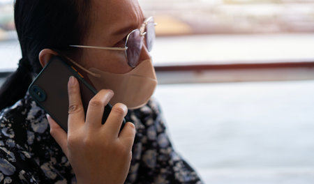 Middle-aged Asian woman looking worried and serious while talking on mobile phone in a port with at sunset.の写真素材