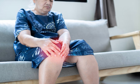 Portrait elderly woman sitting on sofa and suffering from pain her knee, she try to massage, senior healthy conceptの写真素材