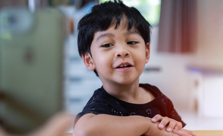 Excited Asian little boy looking at gadget screen or using a smartphone to making selfie photo with happy smiling. Cool Mobile App concept. Selective focus.の写真素材
