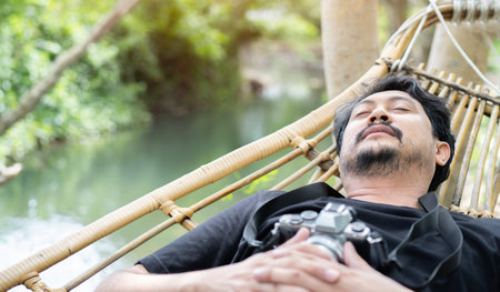 Person sleeping with his camera in a hammock with beautiful summer scene.  Asian man is relaxing in a hammock.の写真素材