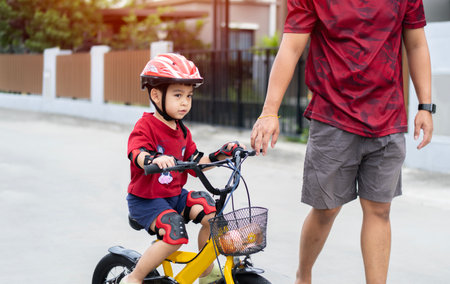 Asian dad teaches son to ride bike, senior helps child, boy in helmet is actively relaxing with his father in the park in summerの写真素材