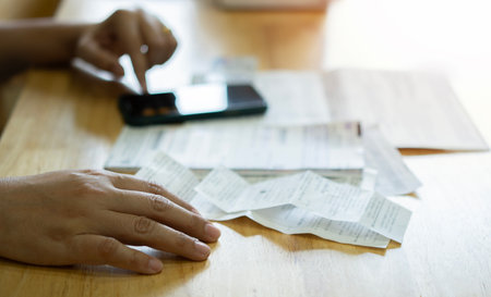 Cropped image of business woman with bills and smart phone at the table. Calculation of costs concept. Selective focus at handの写真素材