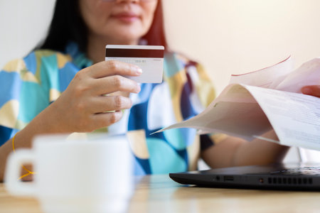 Home office. Close up of young woman owner or renter of dwelling sitting on table before laptop screen making calculations of utility payment holding paper bill and credit card, invoice.の写真素材