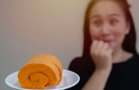 Happy middle aged Asian woman eating orange cake and excited, winner expression celebrating victory screaming with big smile and raised hand. Selective focus, copy space.の写真素材