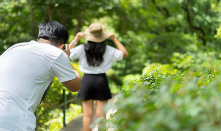 Cropped image of Asian man taking photo of woman on back view  with digital camera in forest on they...