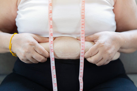An obesity using measuring tape to show the real size. Chubby fat woman using measure tape at belly.の写真素材