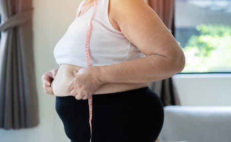 fat woman, fat belly, chubby, obese woman hand holding excessive belly fat with measure tape, woman diet lifestyle conceptの写真素材